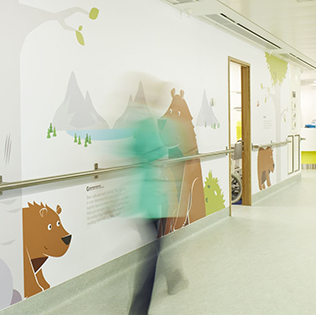 Corridor wall of Bear Ward, decorated with cartoon drawing bears. Staff is seen working in the distance.