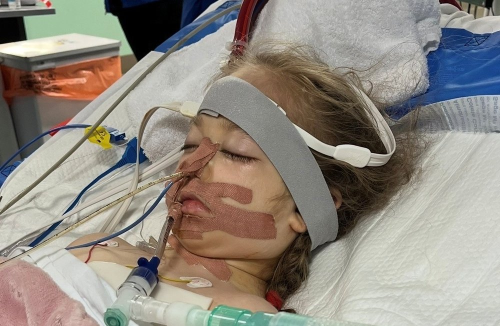a young girl is hooked up to machines and a ventilator in hospital. She looks very poorly.
