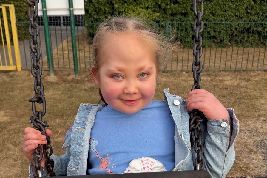 A young girl sits on a swing and smiles