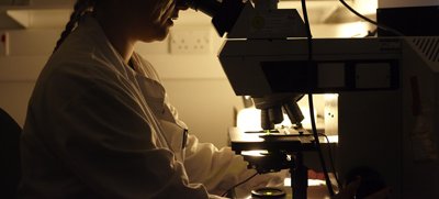 A dark photo of a person looking down a microscope