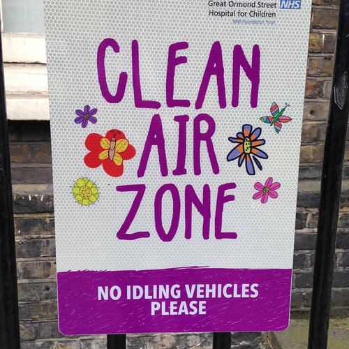 Photo of a sign reading "Clear air zone" and decorated with children's drawings of flowers and butterflies. The caption beneath reads "No idling vehicles please".