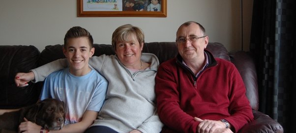 GOSH patient Daniel sitting at home on his sofa with his dog, mum, and dad