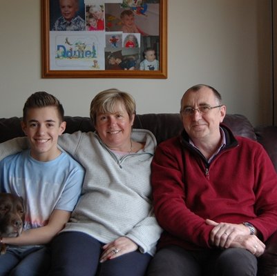 GOSH patient Daniel sitting at home on his sofa with his dog, mum, and dad