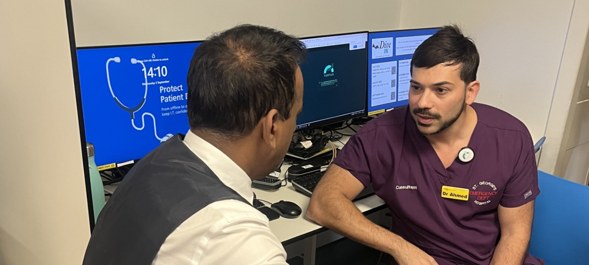 two consultant doctors sat facing each other having conversation with screens behind them
