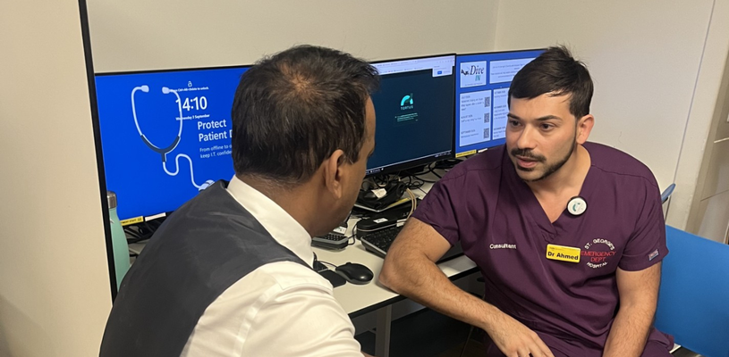 two consultant doctors sat facing each other having conversation with screens behind them
