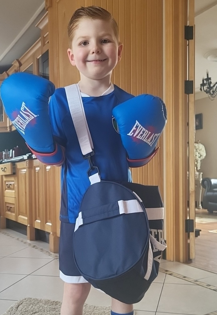 Boy with blue boxing gloves wearing blue sports shorts, t-shirt and trainers