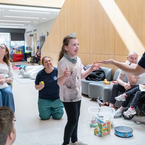 A young girl engages with music and toys while people watch on in the background
