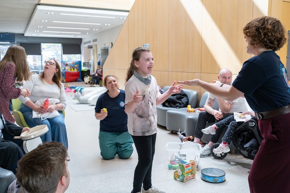 A young girl engages with music and toys while people watch on in the background