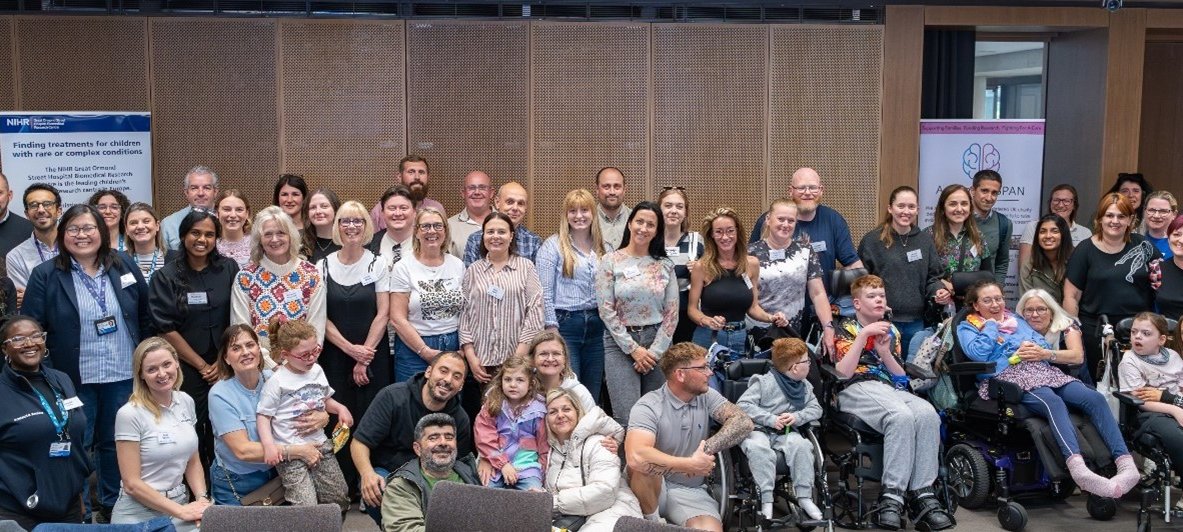 A large group of around 60 people (adults and children) line up and smile at the camera