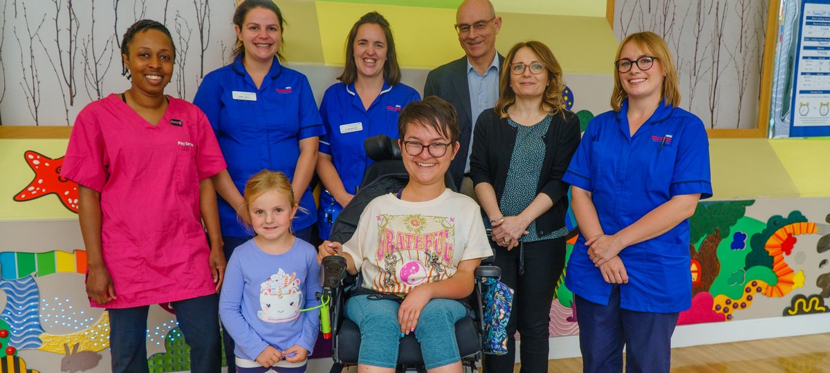 A lady in a wheelchair wearing. She is surrounded by six men and women, and a young girl who wearing a blue top.