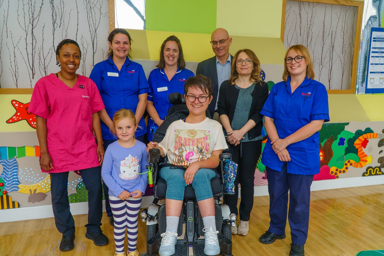 A lady in a wheelchair wearing. She is surrounded by six men and women, and a young girl who wearing a blue top.