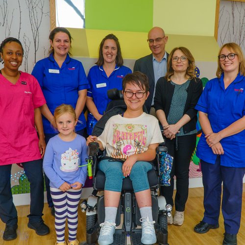 A lady in a wheelchair wearing. She is surrounded by six men and women, and a young girl who wearing a blue top.