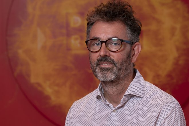 Professor Andrew Taylor, Director of Innovation, wearing shirt and glasses in front of orange DRIVE sign