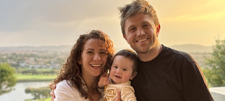 A woman and man are holding a baby with the sunset in the background
