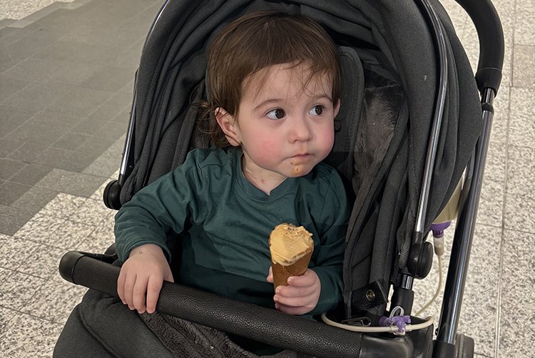 An infant boy is in his black pram and he's holding a big ice cream