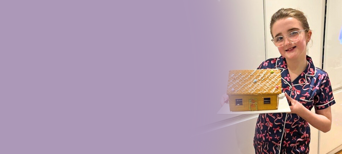 A young girl is holding a gingerbread house cake and smiling