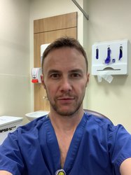 A man looking at the camera wearing dark blue hospital scrubs