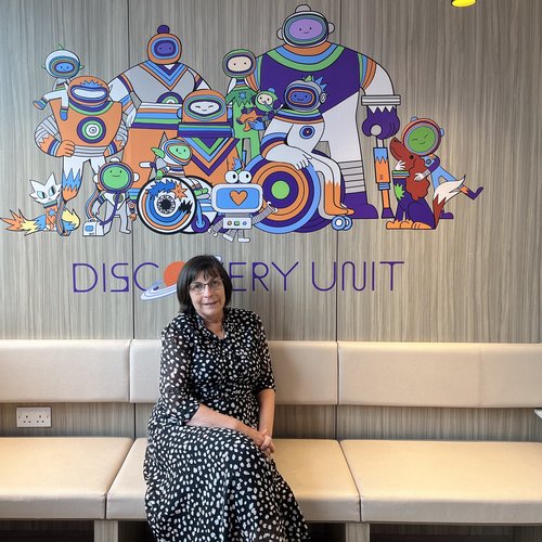 Woman with brown hair sat on white sofa in black and white spotted dress with cartoon space characters in the background