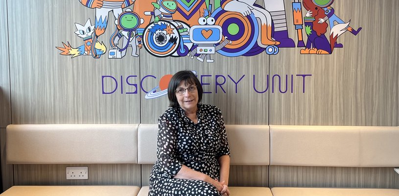 Woman with brown hair sat on white sofa in black and white spotted dress with cartoon space characters in the background