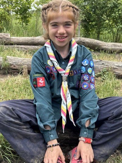 Girl with brown hair sat in scoutting uniform with lots of badges