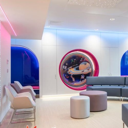 A room with a long blue sofa and pink lights on the wall. There is an illustration of the planets and solar system on the wall.