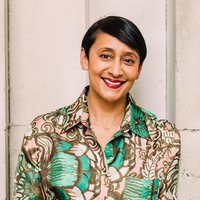 A woman with short brown hair is smiling. She is wearing a pink and green shirt.