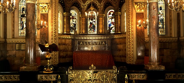 Ornate chapel interior with vaulted ceiling, gilded arches, and stained glass windows. Marble columns and chandeliers create a majestic, reverent ambiance.