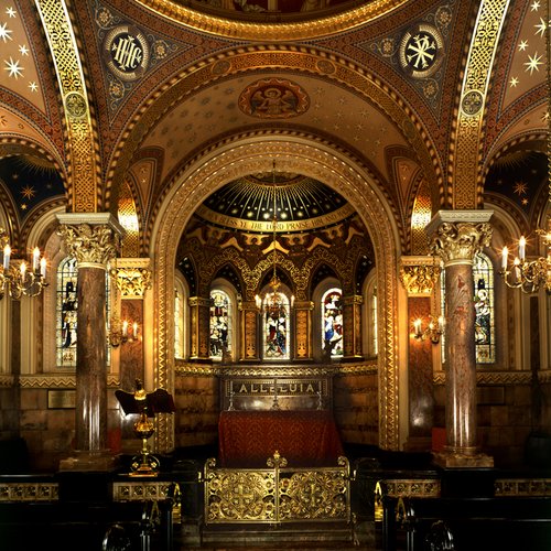Ornate chapel interior with vaulted ceiling, gilded arches, and stained glass windows. Marble columns and chandeliers create a majestic, reverent ambiance.