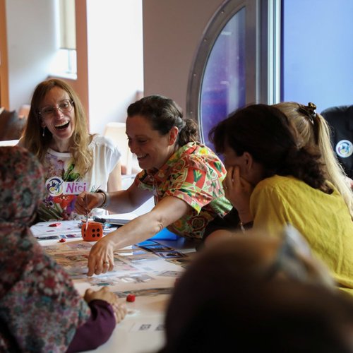 A group of adults are gathered around a table of papers, laughing and interacting