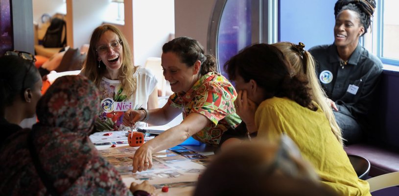 A group of adults are gathered around a table of papers, laughing and interacting