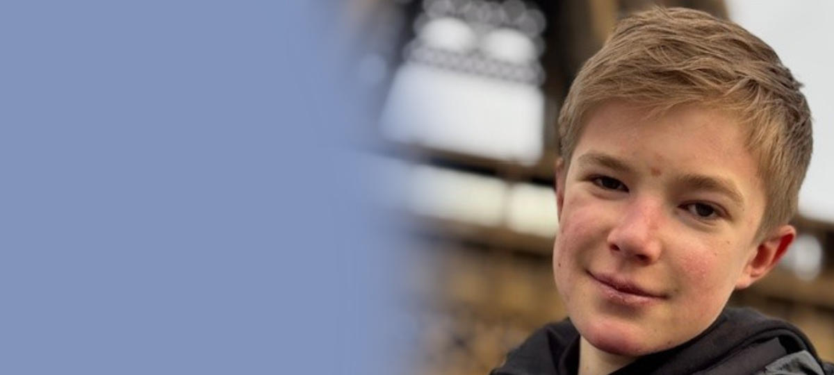A teenage boy smiling at the camera with the Eiffel Tower behind him.