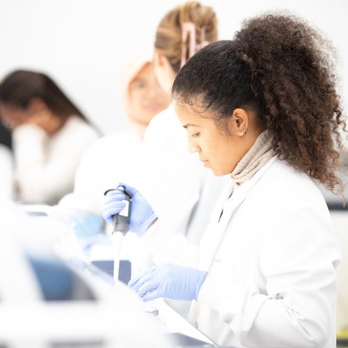 Four researchers wearing lab coats in a line, with the staff member at the front holding a pipette