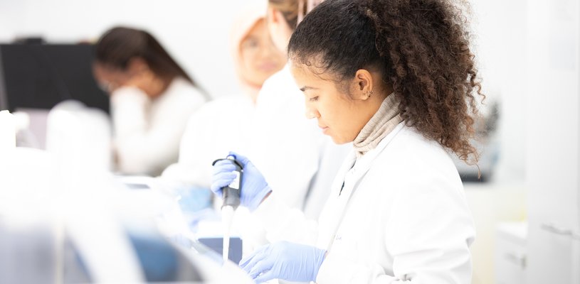 Four researchers wearing lab coats in a line, with the staff member at the front holding a pipette