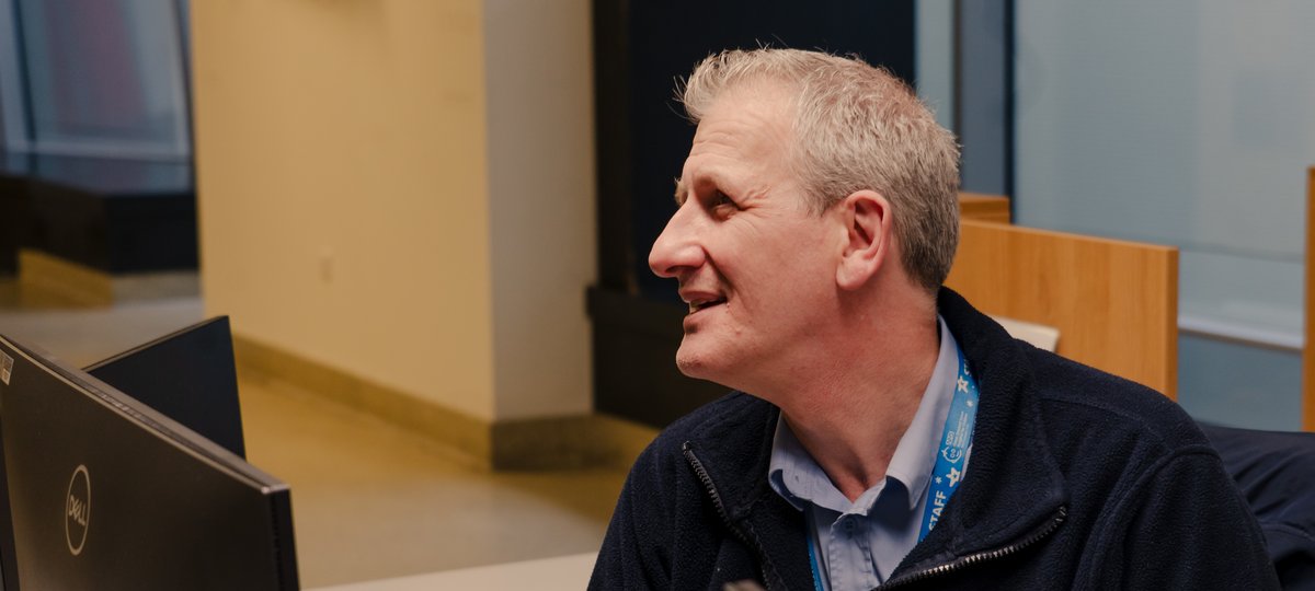 A man with grey hair sat behind a computer screen