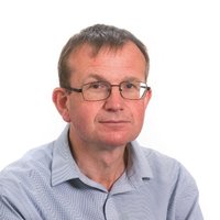 A man wearing a blue shirt and black glasses is smiling