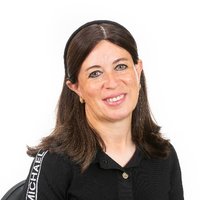 A woman with short brown hair, wearing a black shirt, is smiling.