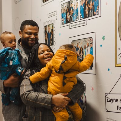 Zayne and Zion with their mum and dad standing before their family wall.