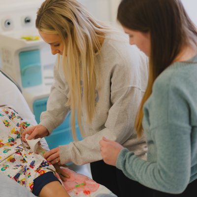 Two students work with a training dummy in a simulation designed to train them in nursing skills.