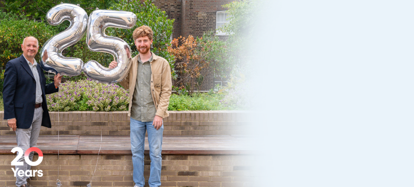 Professor Adrian Thrasher standing next to Rhys holding silver 25 balloons in front of a garden