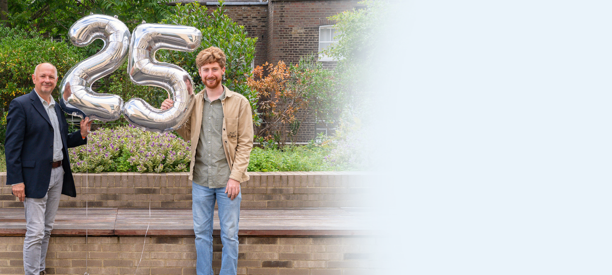 Two men standing holding big 25 balloons