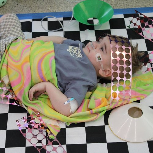 A child laying on a play mat with a blanket over them
