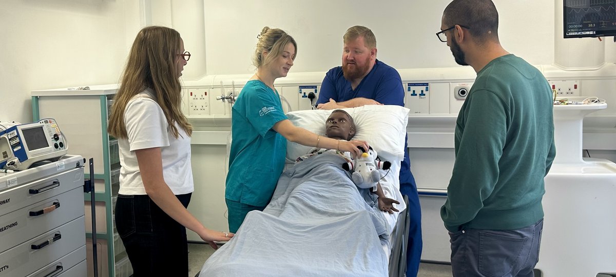 Four hospital staff members standing around a hospital bed that has a manakin laying in it