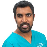 A man with dark hair and a beard, wearing a blue t-shirt is smiling