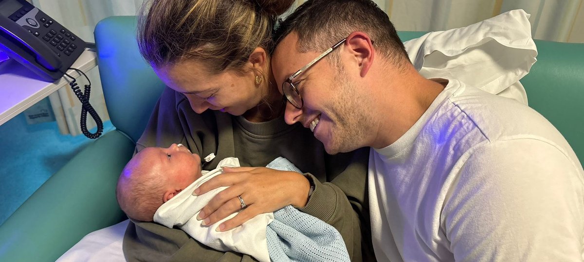 A baby cuddles up with his parents and everyone is smiling