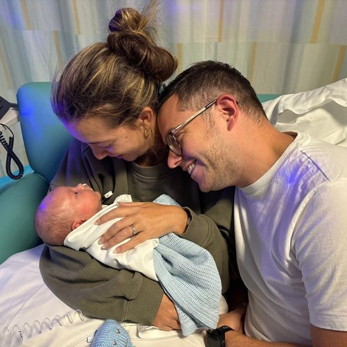 A baby cuddles up with his parents and everyone is smiling