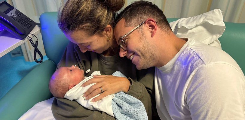 A baby cuddles up with his parents and everyone is smiling