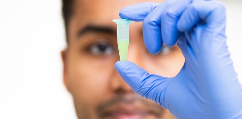 A close up image of a vial of liquid with a blurry outline of the man holding it behind