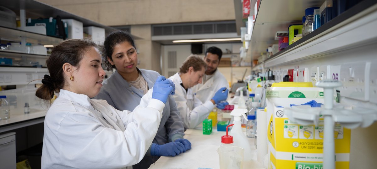 Four people wearing lab coats holding pipettes