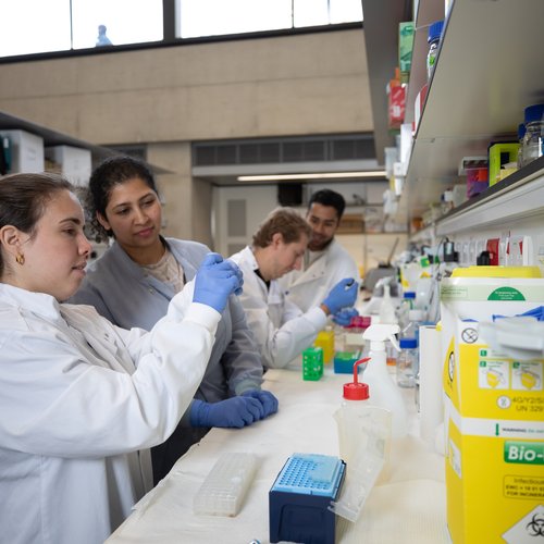 Four people wearing lab coats holding pipettes