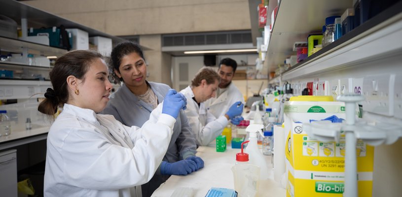 Four people wearing lab coats holding pipettes